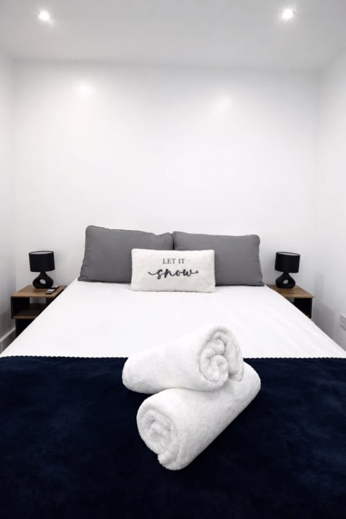 Modern bedroom at La Rose Serenity Residence with white bed, rolled white towels, 'Let it snow' pillow, and black bedside