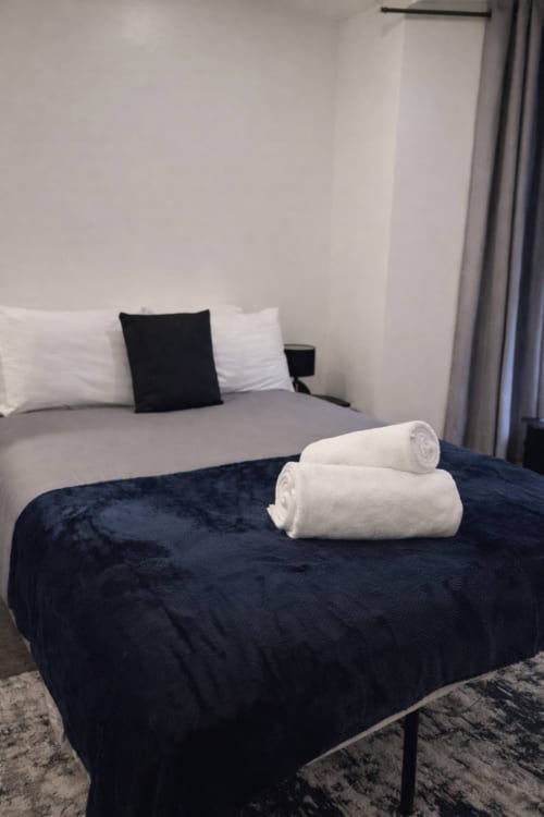 Modern bedroom at La Rose Serenity Residence with navy bed, rolled white towels, black and white pillows, grey curtains in