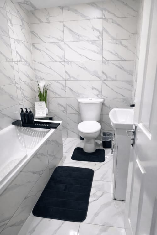 Modern marble bathroom at La Rose Serenity Residence, London B&B with white fixtures, black bath mats, and minimalist décor
