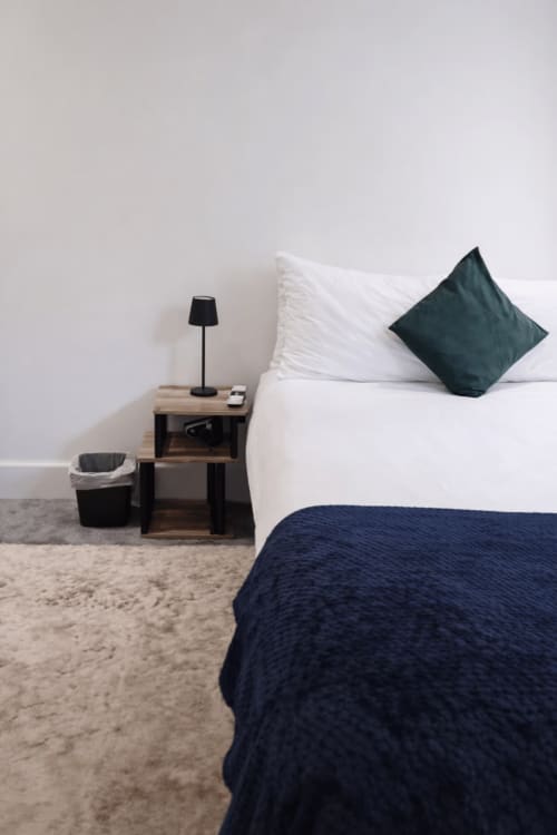 Modern bedroom at La Rose Serenity Residence London with white pillows, dark teal cushion, navy blanket, wooden nightstand