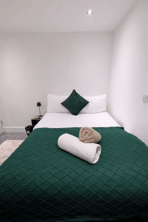 Modern bedroom at La Rose Serenity Residence with emerald green quilted bed, white pillows, rolled towels, and minimalist