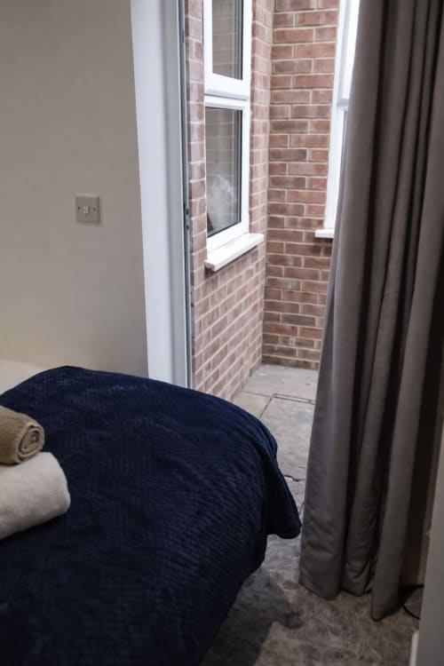 Bedroom with brick exterior view from window, navy bedding, and taupe curtains at La Rose Serenity Residence in London
