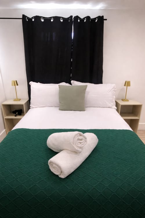 Modern bedroom at La Rose Serenity Residence London with queen bed, rolled white towels, green throw, black curtain