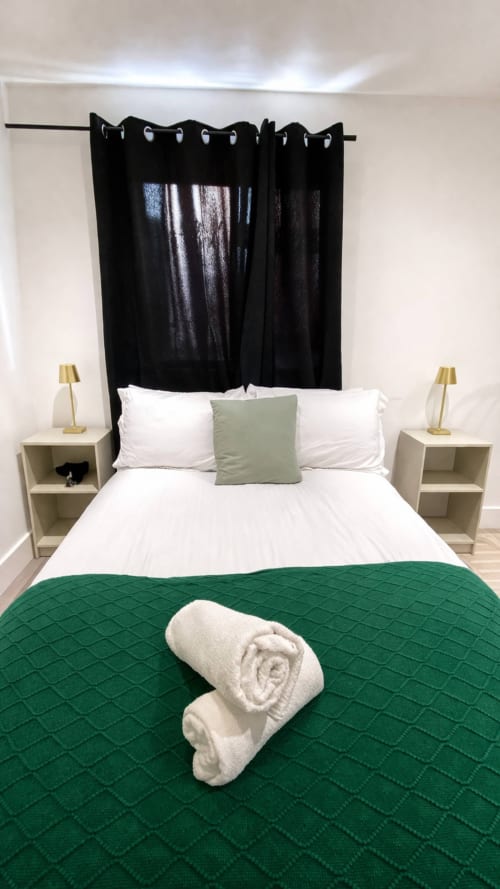 Modern bedroom at La Rose Serenity Residence with green quilt, white bedding, black curtain headboard, and rolled towel