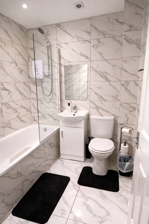 Modern marble bathroom at La Rose Serenity Residence, London. Features walk-in shower, vanity sink, toilet, and black bath