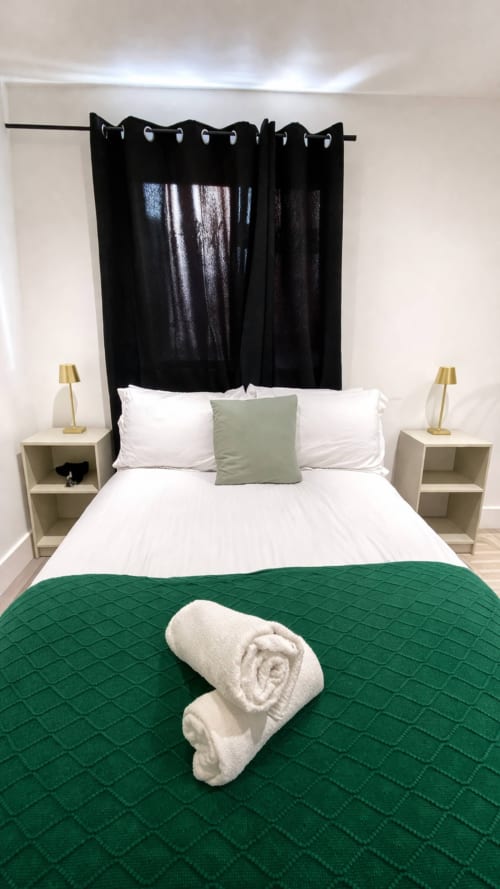 La Rose Serenity Residence elegant bedroom with black curtains, white bedding, green quilt, rolled towels, and gold lamps in