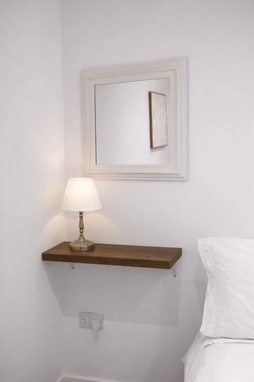 Elegant bedroom corner at La Rose Serenity, London with mirrored wall shelf, brass lamp, and white bedding