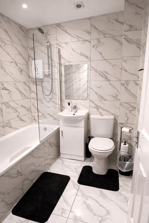 Modern marble bathroom at La Rose Serenity Residence with walk-in shower, dual sink vanity, and black bath mats in London