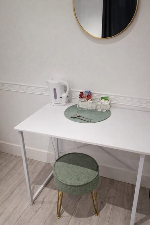 Elegant hotel room workspace at La Rose Serenity Residence with white desk, green stool, kettle, and round mirror in London