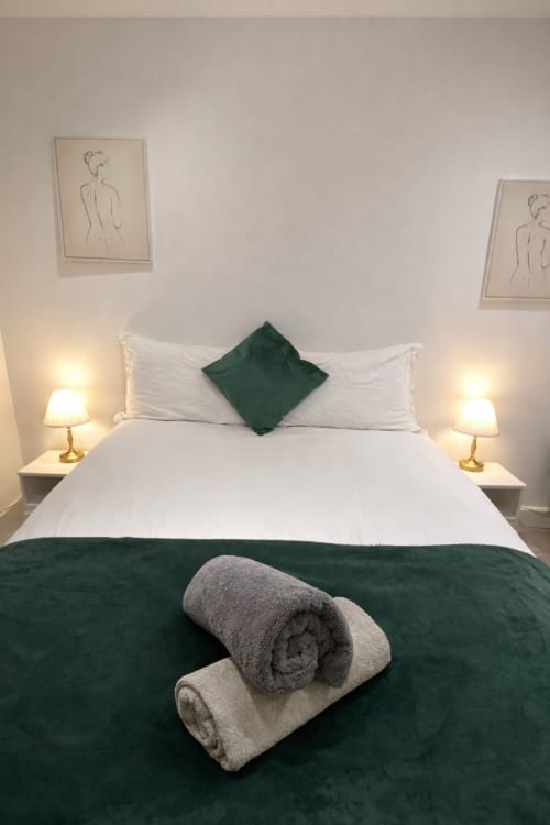 Elegant bedroom at La Rose Serenity Residence in London with green accents, white bedding, rolled towels, and artistic