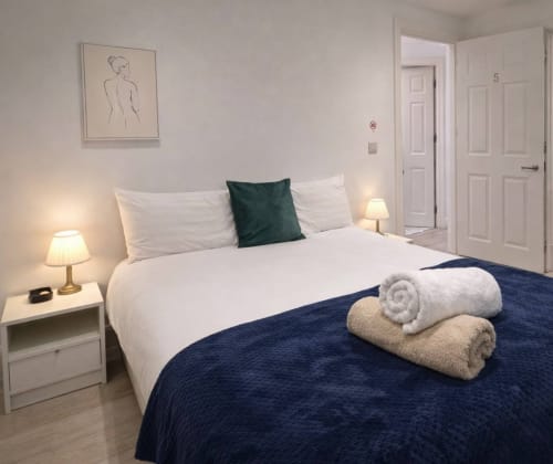 Modern bedroom at La Rose Serenity Residence with queen bed, white linens, teal pillow, rolled towels, and bedside lamps in