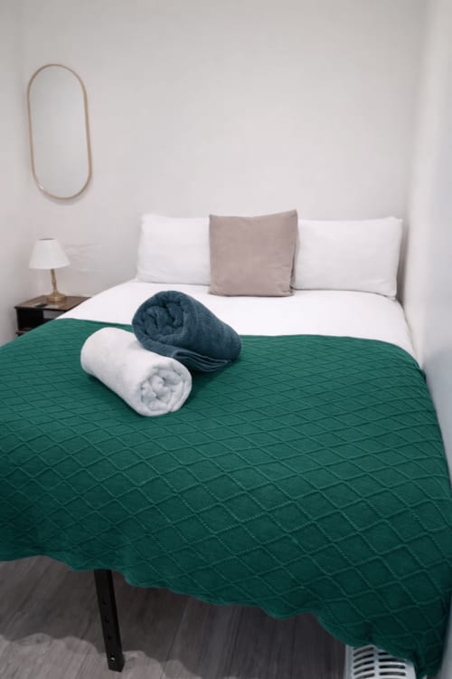 Elegant bedroom at La Rose Serenity Residence with green quilted throw, white pillows, and rolled towels on bed