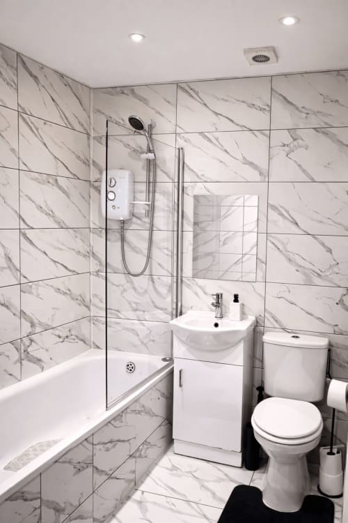 Modern marble bathroom at La Rose Serenity Residence in London with walk-in shower, toilet, and pedestal sink