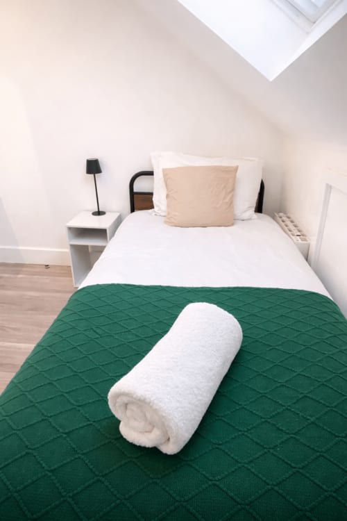 Cozy London B&B room with green quilted throw on white bedding, rolled towel, and minimalist decor at La Rose Serenity