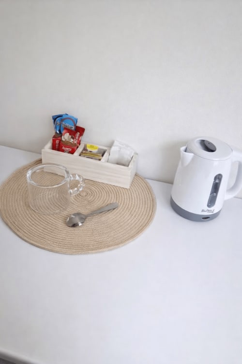 Hotel room desk setup with kettle, circular woven placemat, glass mug, and wooden organizer with supplies at La Rose Serenity