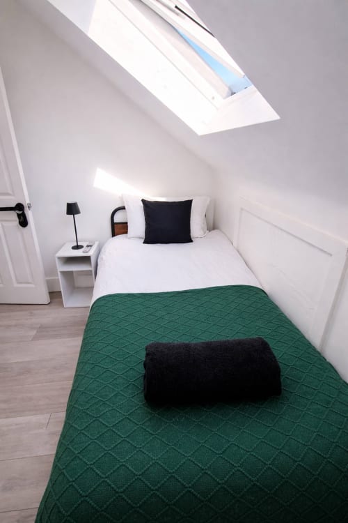 Modern attic bedroom at La Rose Serenity Residence with skylight, white walls, single bed, green quilt, and minimalist decor