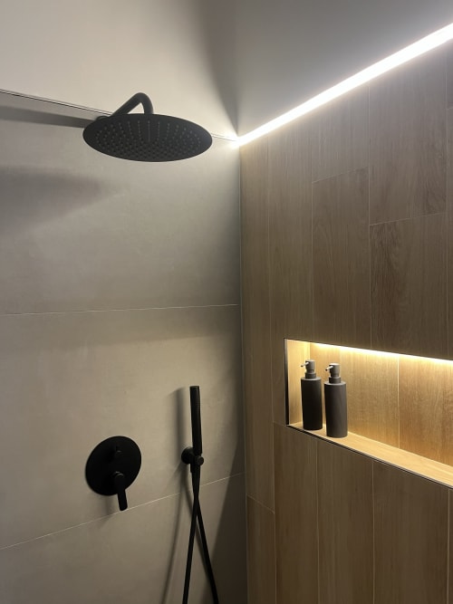Doccia moderna con soffione nero, comandi a muro e rivestimento in legno con scaffale illuminato