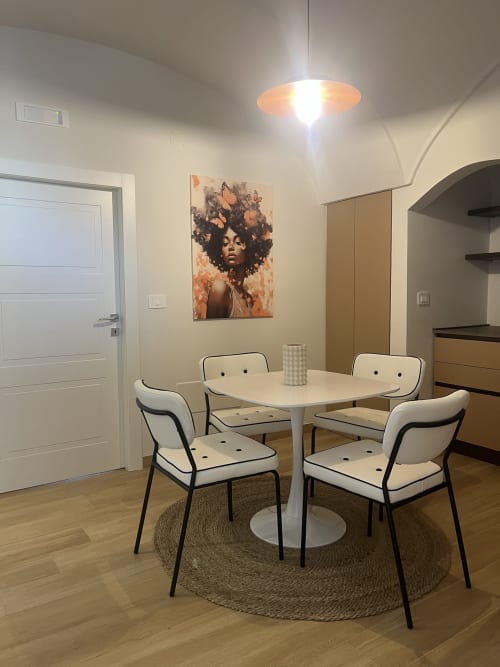 Moderna zona pranzo nell'appartamento Marelia Suites con tavolo bianco rotondo, quattro sedie e opere d'arte a farfalla su pareti beige