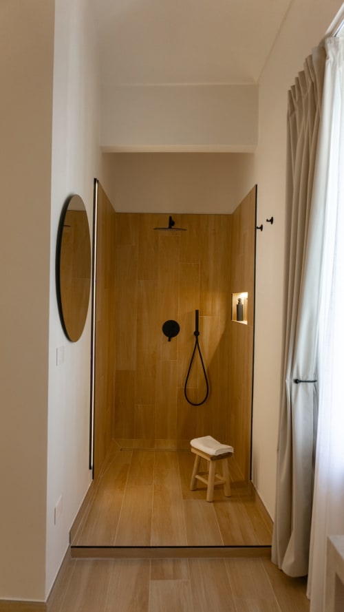 Bagno moderno alle Marelia Suites con doccia in piastrelle effetto legno, rubinetteria nera e sgabello in legno nell'appartamento italiano