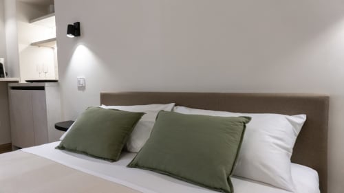 Camera moderna di Marelia Suites con cuscini verdi, biancheria bianca e testiera beige nell'appartamento italiano