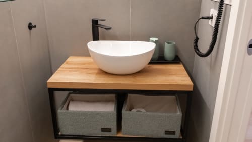 Elegante bagno con lavabo rotondo bianco, piano in legno, rubinetto nero e cestini contenitori presso Marelia Suites