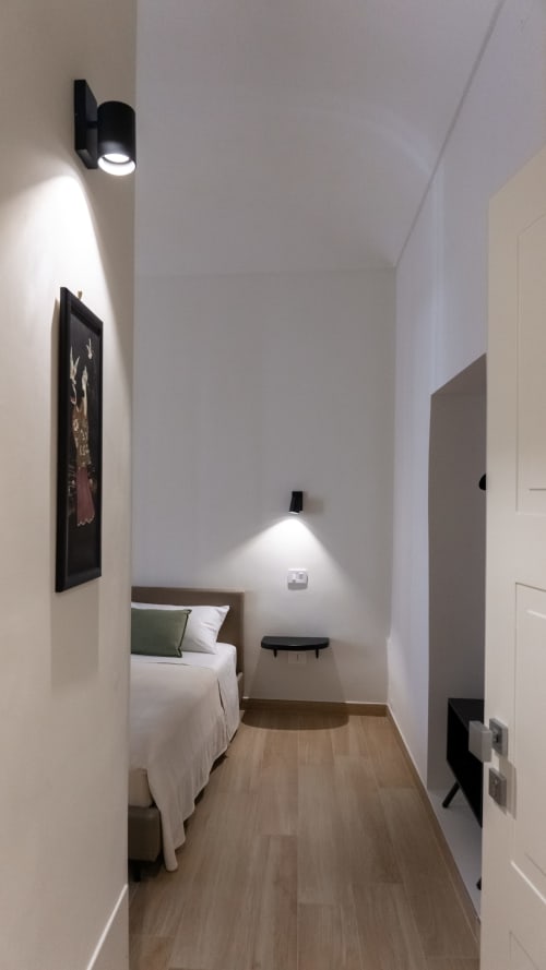 Camera da letto stretta alle Marelia Suites con letto singolo, pavimenti in legno, luci a parete e design minimalista moderno