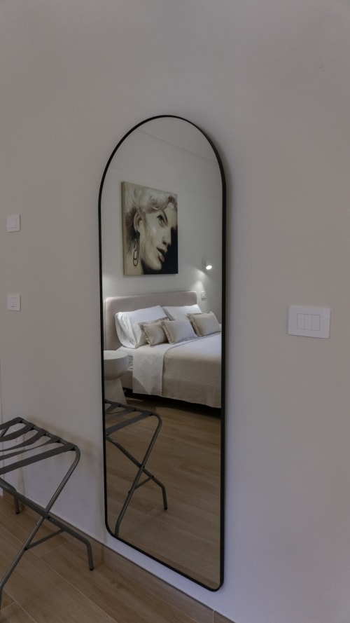 Specchio ad arco con cornice nera che riflette la camera moderna della suite Marelia in Italia