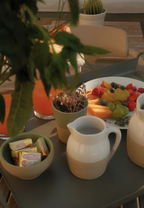 Table de petit-déjeuner au Moulin Renaudiots avec fruits frais, pâtisseries, plantes et service de café dans une pièce ensoleillée