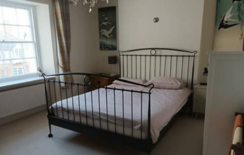 Bedroom at 2 Doves Holiday Property in Exeter featuring black metal bed frame with pink bedding, window with garden view, and