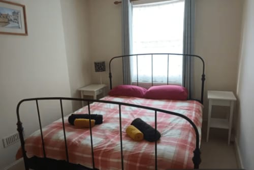 Bedroom with black metal bed frame, pink checkered bedding, burgundy pillows, and window with garden view at 2 Doves Holiday