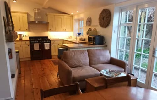 Open-plan kitchen and sitting area at Clara Place cottage in Exeter, with wooden floors, beige cabinetry, black range cooker,