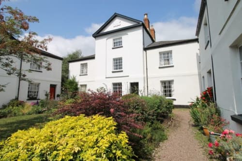 2 Doves Holiday Property cottage in Exeter with white exterior, terracotta chimneys, and colorful garden featuring yellow and