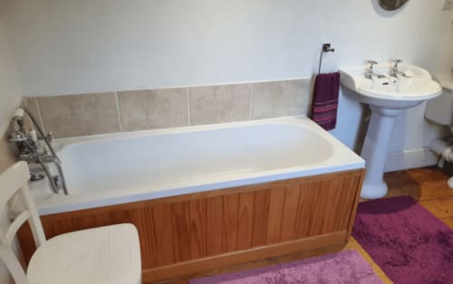 Bathroom at 2 Doves Holiday Property cottage in Exeter with wooden bathtub, pedestal sink, and purple bathmat