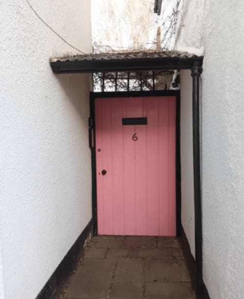 Pink door numbered 6 at Clara Place cottage entrance in Exeter with black frame and covered porch