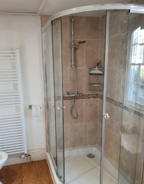 Modern glass shower enclosure with rainfall showerhead and storage shelves in Clara Place cottage bathroom at 2 Doves Holiday