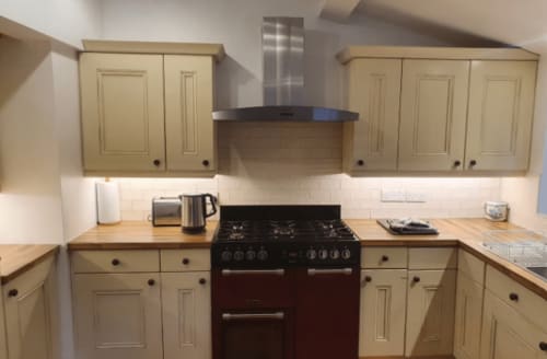 Cream kitchen with dark red range cooker, gas hob, stainless steel extractor hood, and wood countertops in Clara Place