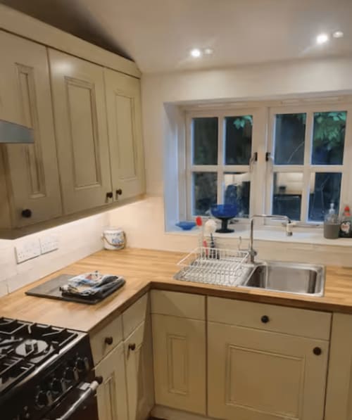 Modern cream kitchen with wooden worktops, stainless steel sink, gas hob, and garden view windows at Clara Place cottage,