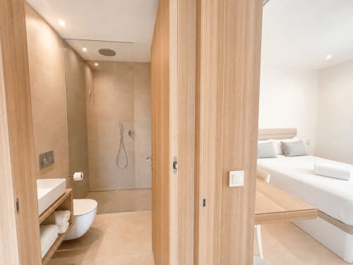 Baño moderno en suite del apartamento Holibai en Baiona con ducha a ras de suelo, inodoro, lavamanos y acabados en madera