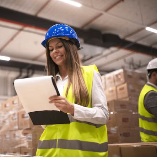 Gerente de almacén con casco azul y chaleco de seguridad verificando inventario en tableta en la instalación de almacenamiento de Zaragoza