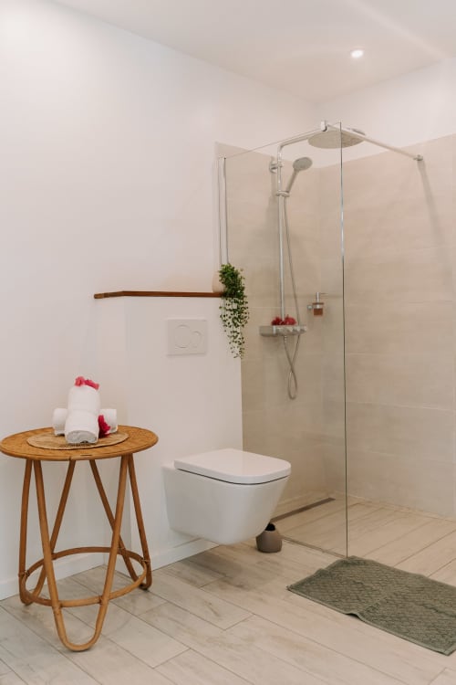 Modern bathroom at Habitation I'SEO with walk-in shower, wall-mounted toilet, wooden side table with towels, and minimalist