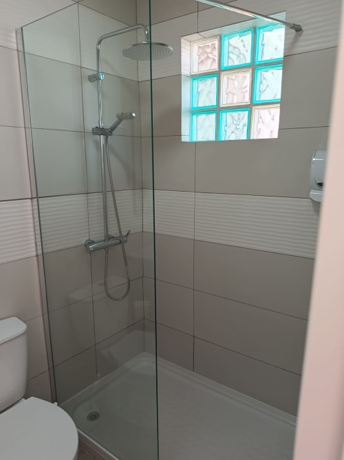 Chuveiro moderno com divisória de vidro, chuveiro tipo chuva e janela de blocos de vidro turquesa no quarto Alfarroba em Cerro da Janela