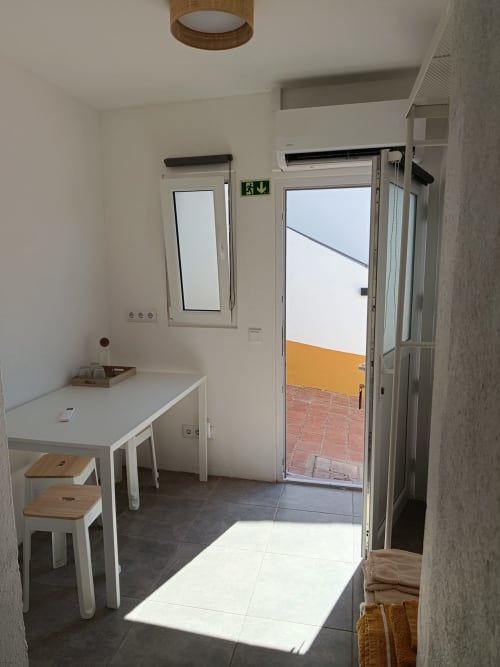 Cozinha clara da pousada Cerro da Janela com mesa branca, bancos e portas para a varanda
