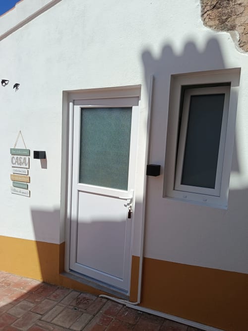 Porta e janela de entrada brancas do Cerro da Janela Hostel em Alte, Portugal, com rodapé amarelo e pátio