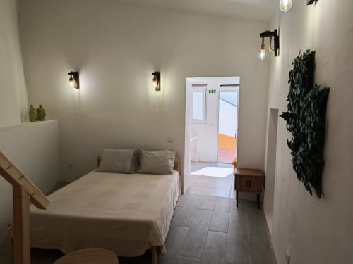 Quarto do Hostel Cerro da Janela em Alfarraba com cama, arandelas de parede, plantas em vasos e porta aberta para o corredor