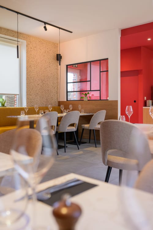 Modern restaurant dining room at B&B Sens'UP with gray chairs, cork wall, red accent wall, and elegant table settings near