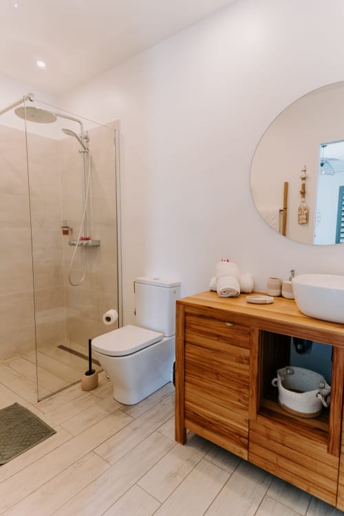 Salle de bain moderne à l'Habitation I'SEO avec douche ouverte, meuble vasque en bois, miroir rond et sanitaires blancs
