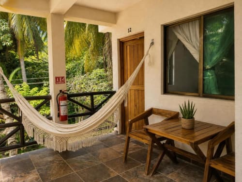 Balcón de la Suite 12 en Hotel Holbox Centro con hamaca, mesa de madera y vistas a un exuberante jardín tropical en Holbox, México
