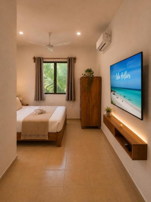 Habitación moderna del Hotel Holbox Centro en Holbox, México con cama, muebles de madera y televisor mostrando una playa