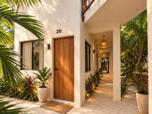 Entrada de la Suite 20 en Hotel Holbox Centro con puerta de madera, plantas tropicales y camino arenoso en Holbox, México