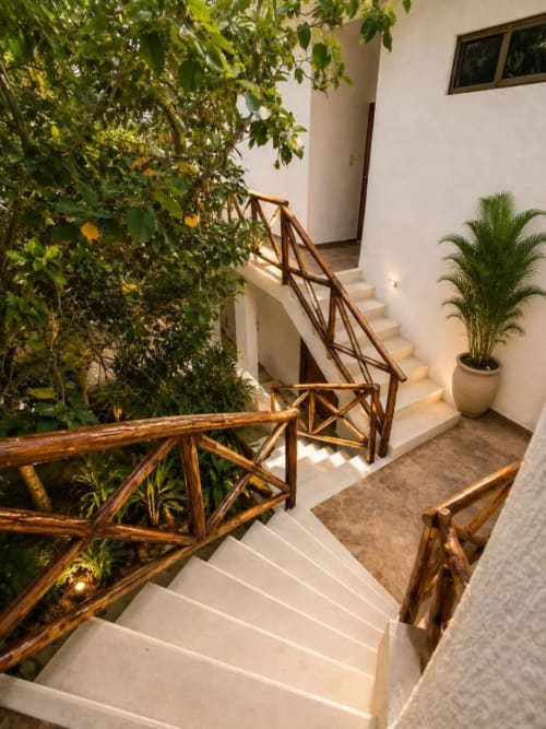 Escalera interior del Hotel Holbox Centro con exuberante vegetación, barandillas de madera y palmera en maceta en la suite Holbox.